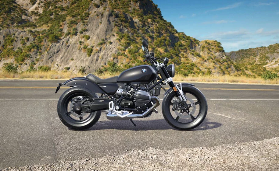 Schwarzes BMW Motorrad parkt auf einer Straße vor einer felsigen Bergkulisse.