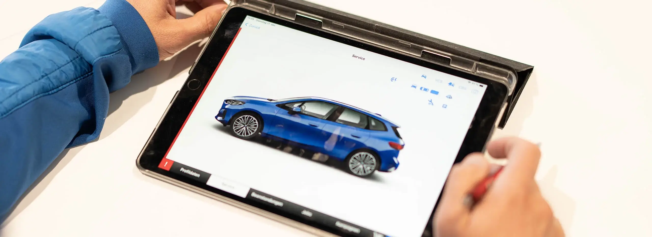 Eine Person hält ein Tablet, das ein blaues Auto und Service-Informationen anzeigt.