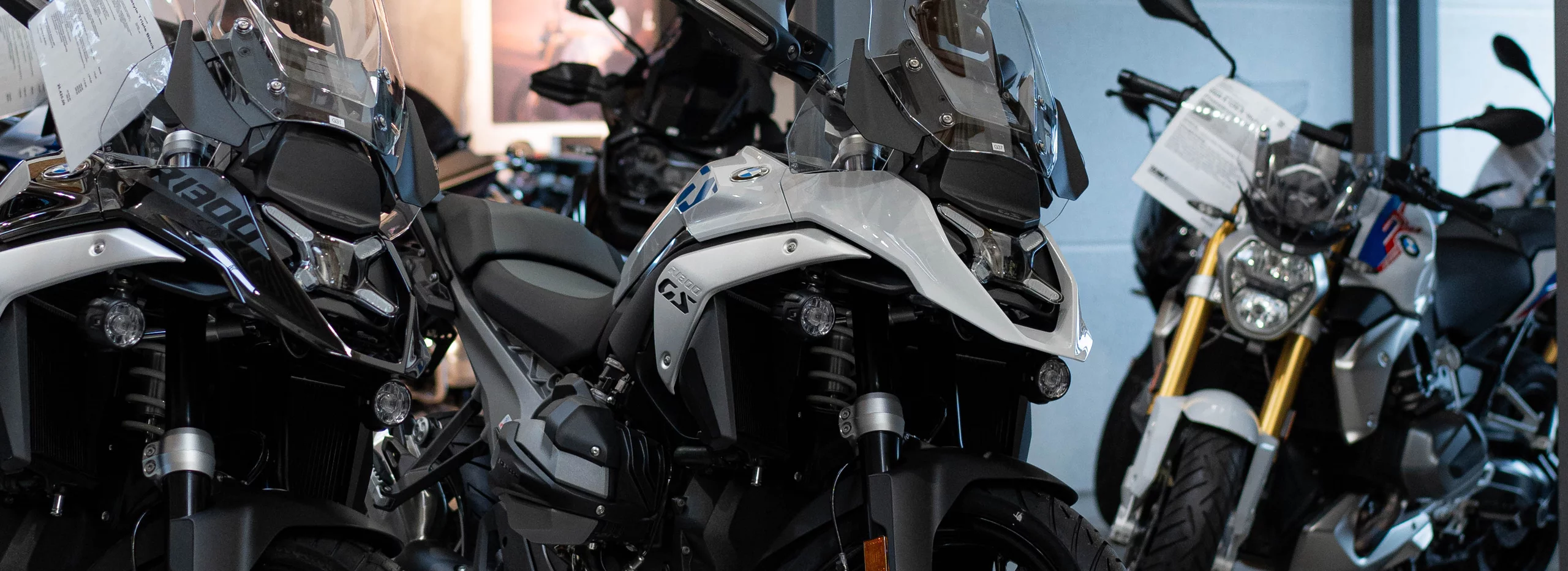 Drei BMW GS Motorräder in einem Showroom, mit einem silber-weißen Modell im Vordergrund.