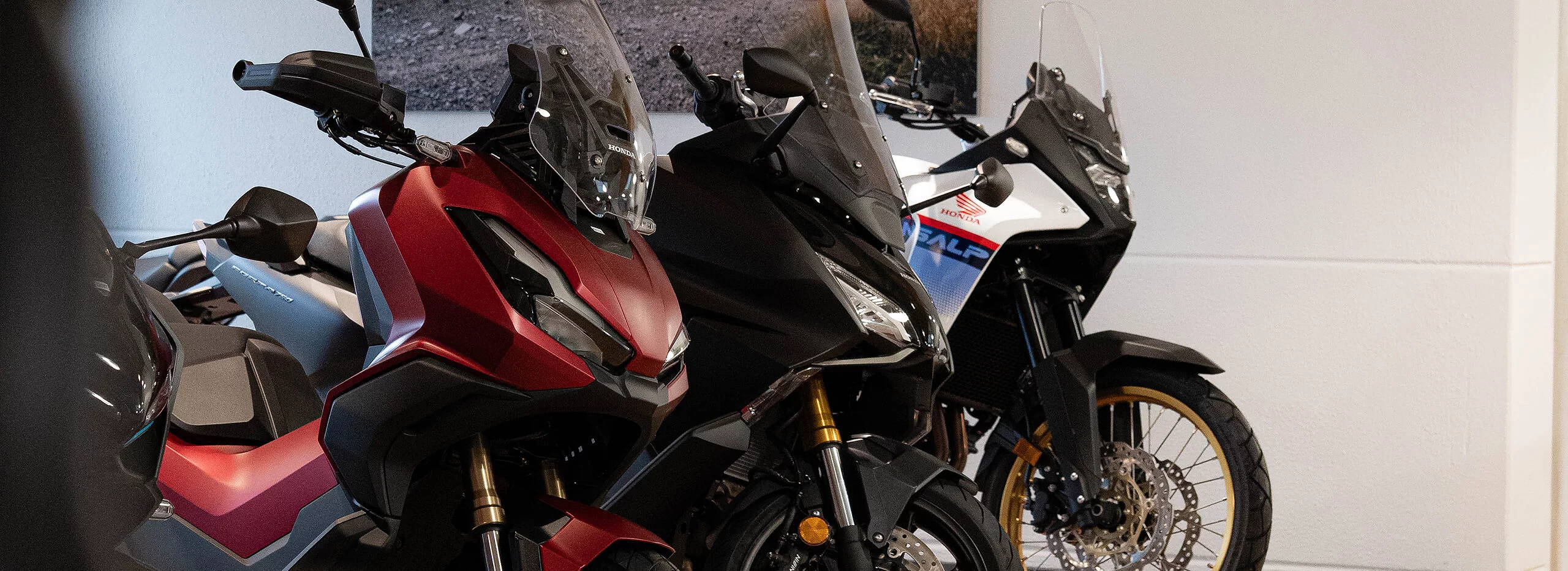 Drei Honda Motorräder und Roller (rot, schwarz, weiß) stehen in einem Showroom.