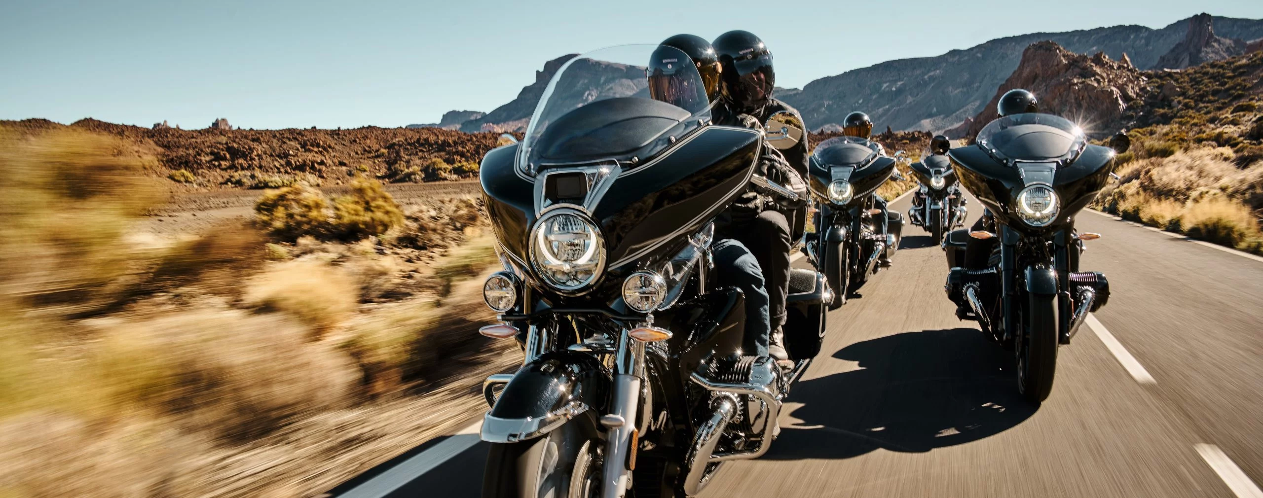  Eine Reihe von Motorradfahrern auf schwarzen Cruisern fährt durch eine Wüstenlandschaft.