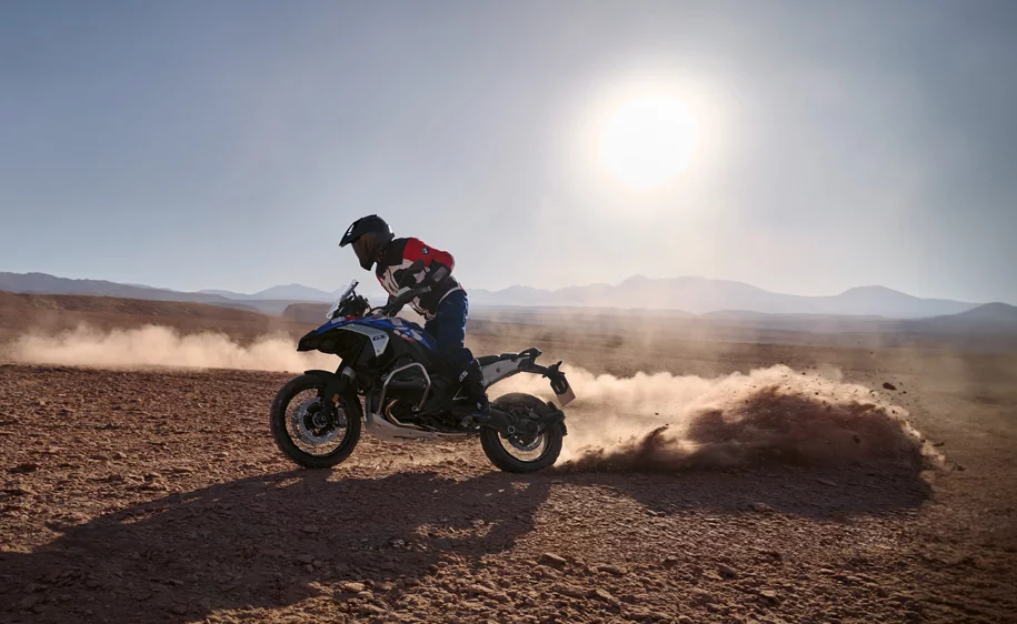 Motorradfahrer auf einer BMW R 1300 GS Adventure in einer staubigen Wüstenlandschaft bei Sonnenuntergang