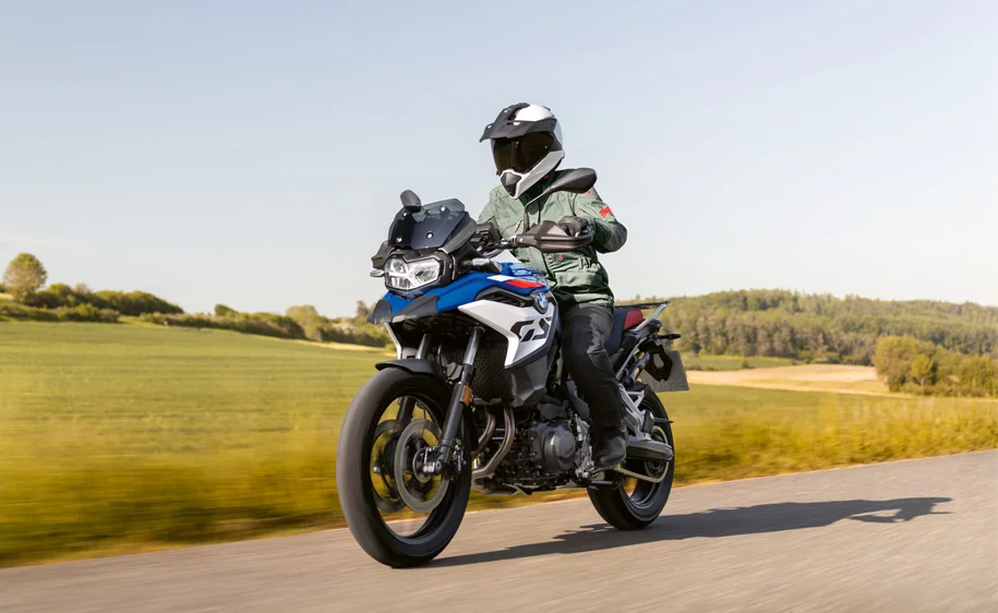 Motorradfahrer auf einer blau-weißen BMW F 800 GS fährt auf einer Landstraße durch grüne Landschaft.