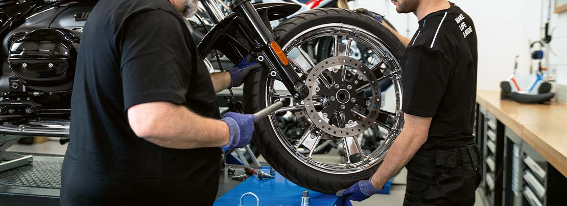 2 Mechaniker arbeiten in einer Werkstatt an einem Rad von einem Motorrad