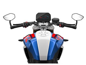 Das Bild zeigt die Fahrerperspektive auf das Cockpit des Motorrads. Man sieht den breiten Lenker mit den Armaturen, Griffen und den beiden eckigen Rückspiegeln. Zentral platziert ist das digitale TFT-Display mit Grafiken in Rot und Blau. Der Kraftstofftank davor ist in Weiß, Blau und Rot lackiert, passend zum sportlichen M-Design.