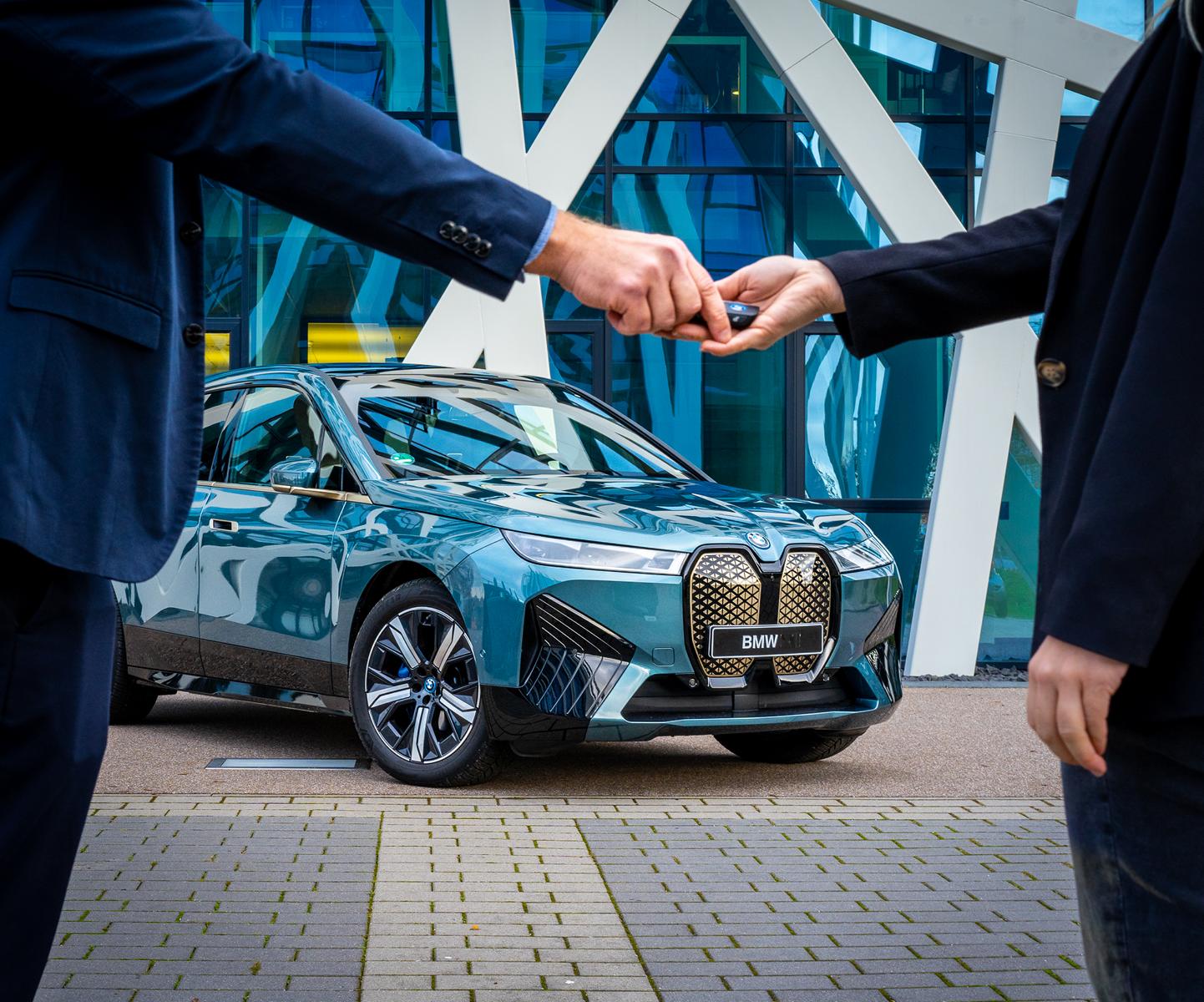 Schlüsselübergabe eines blauen BMW iX vor modernem Gebäude