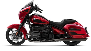 Ein glänzendes, rotes BMW-Motorrad im Bagger-Stil. Es steht schräg von der Seite vor einem weißen Hintergrund. Es ist mit einer kleinen Windschutzscheibe, einer Verkleidung und seitlichen Koffern ausgestattet, die alle im gleichen Rotton gehalten sind. Der Motor und der Rahmen sind schwarz.