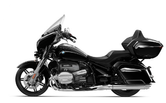  Ein großes, schwarzes Motorrad von BMW im Touring-Stil. Es steht schräg von der Seite vor einem weißen Hintergrund. Das Motorrad ist mit einer großen Windschutzscheibe, seitlichen Koffern und einem Topcase ausgestattet. Es hat verchromte Auspuffrohre auf der rechten Seite.